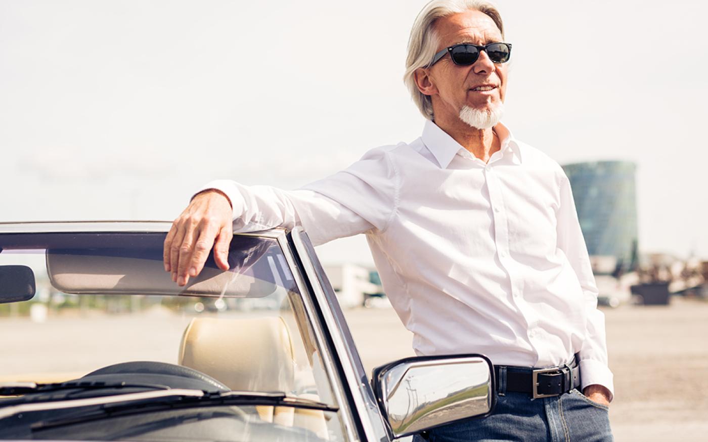 old man posing by car